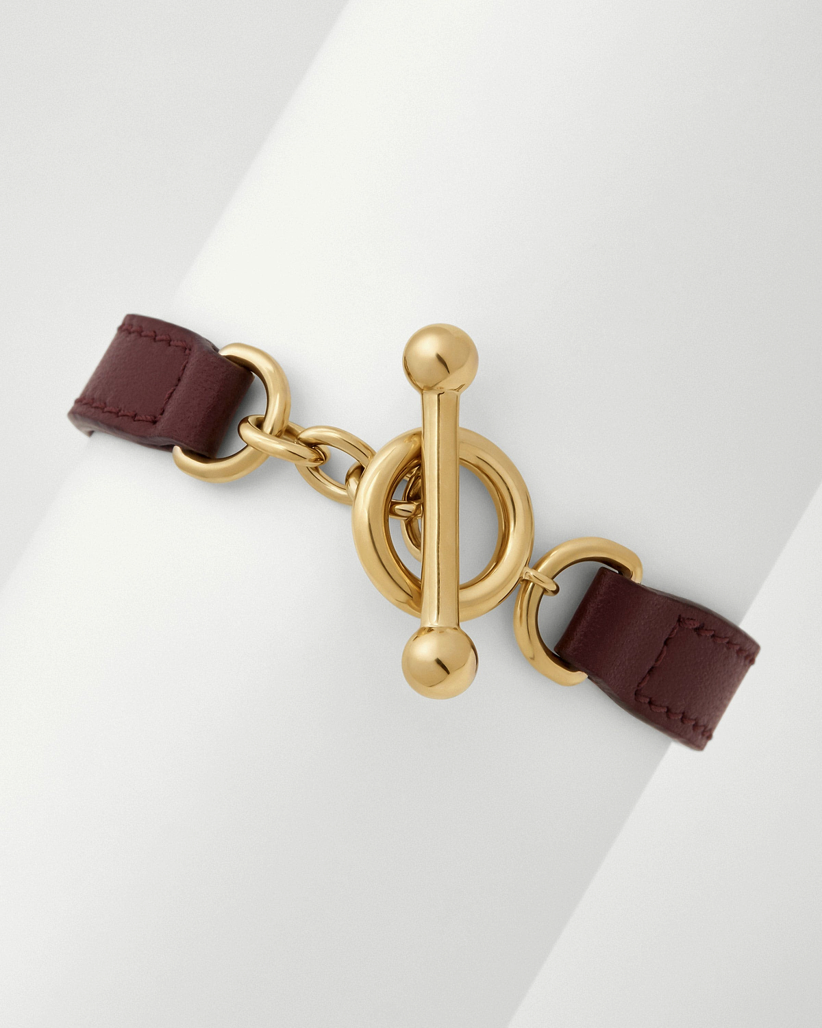 Oxblood leather kite bracelet with gold toggle clasp on white background