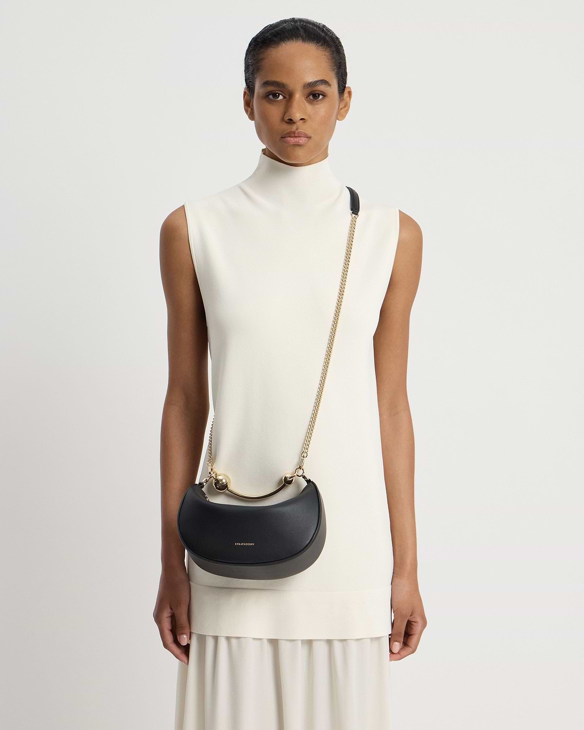 Model wearing black Strathberry Crescent Moon Mini shoulder bag with gold hardware