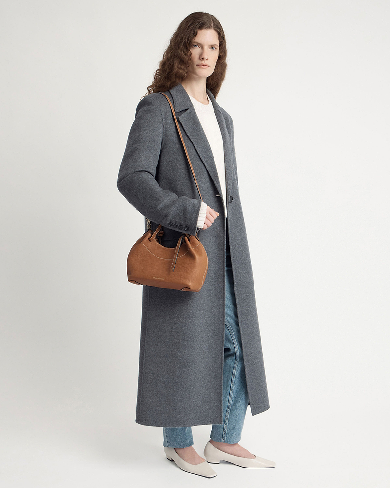 Model wearing grey coat with tan Barra Mini shoulder bag.