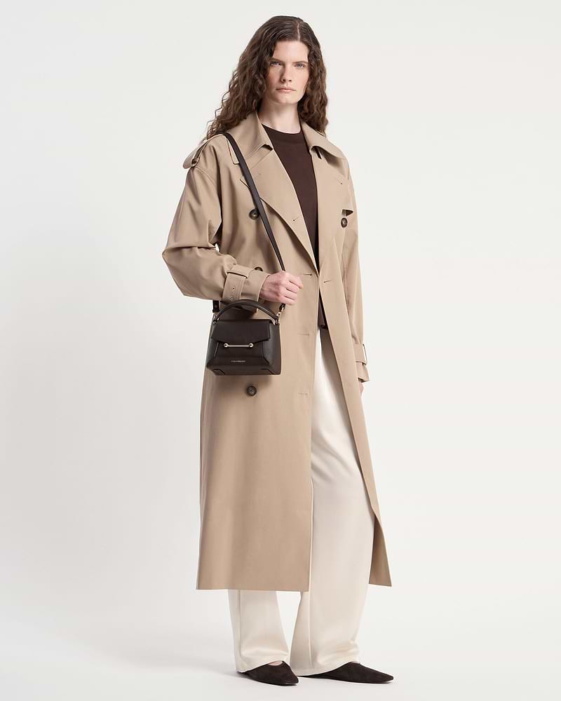 Model wearing a beige trench coat holding an espresso Mosaic Nano bag with shoulder strap.