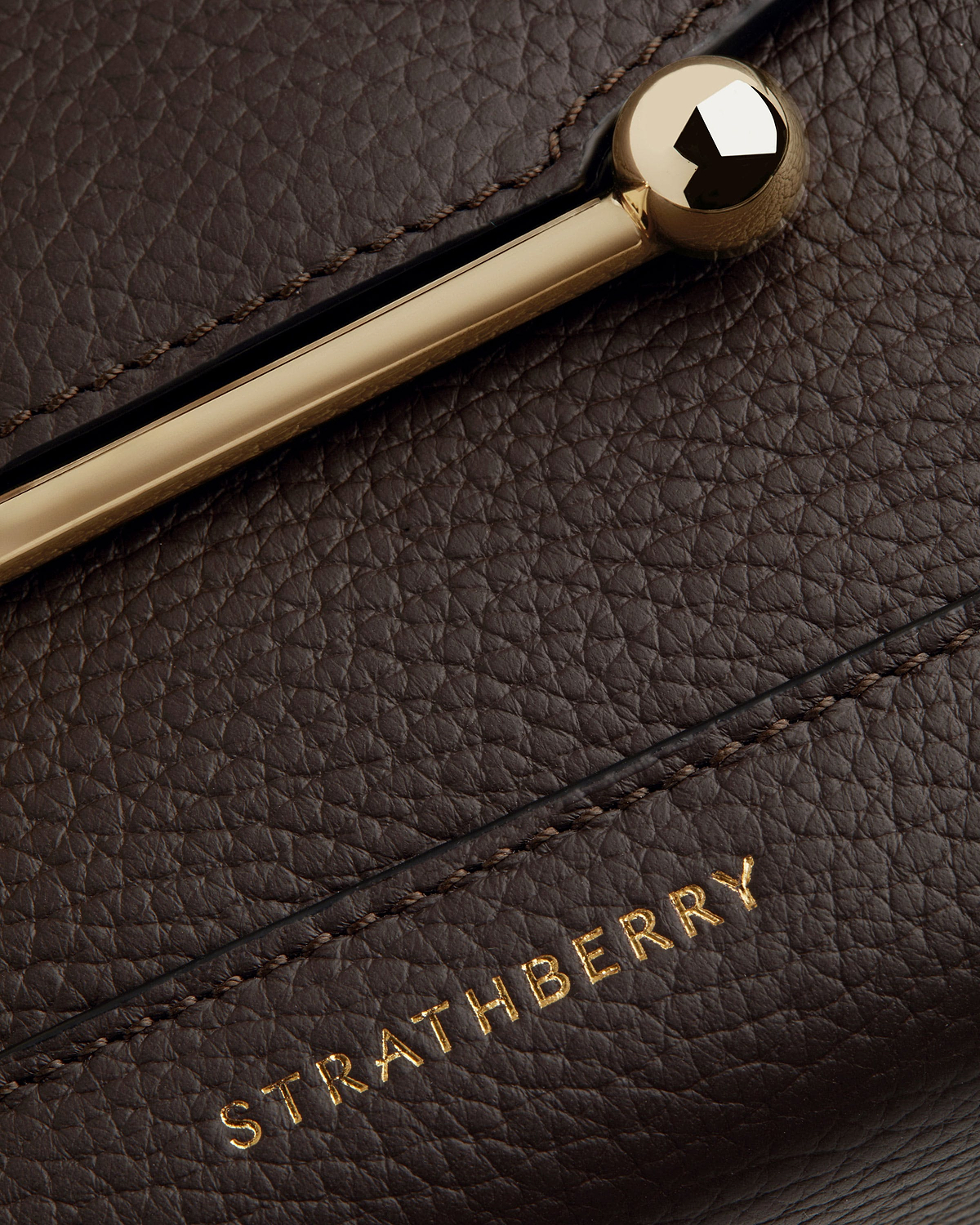 Close up of espresso pebbled leather and gold bar clasp with Strathberry logo