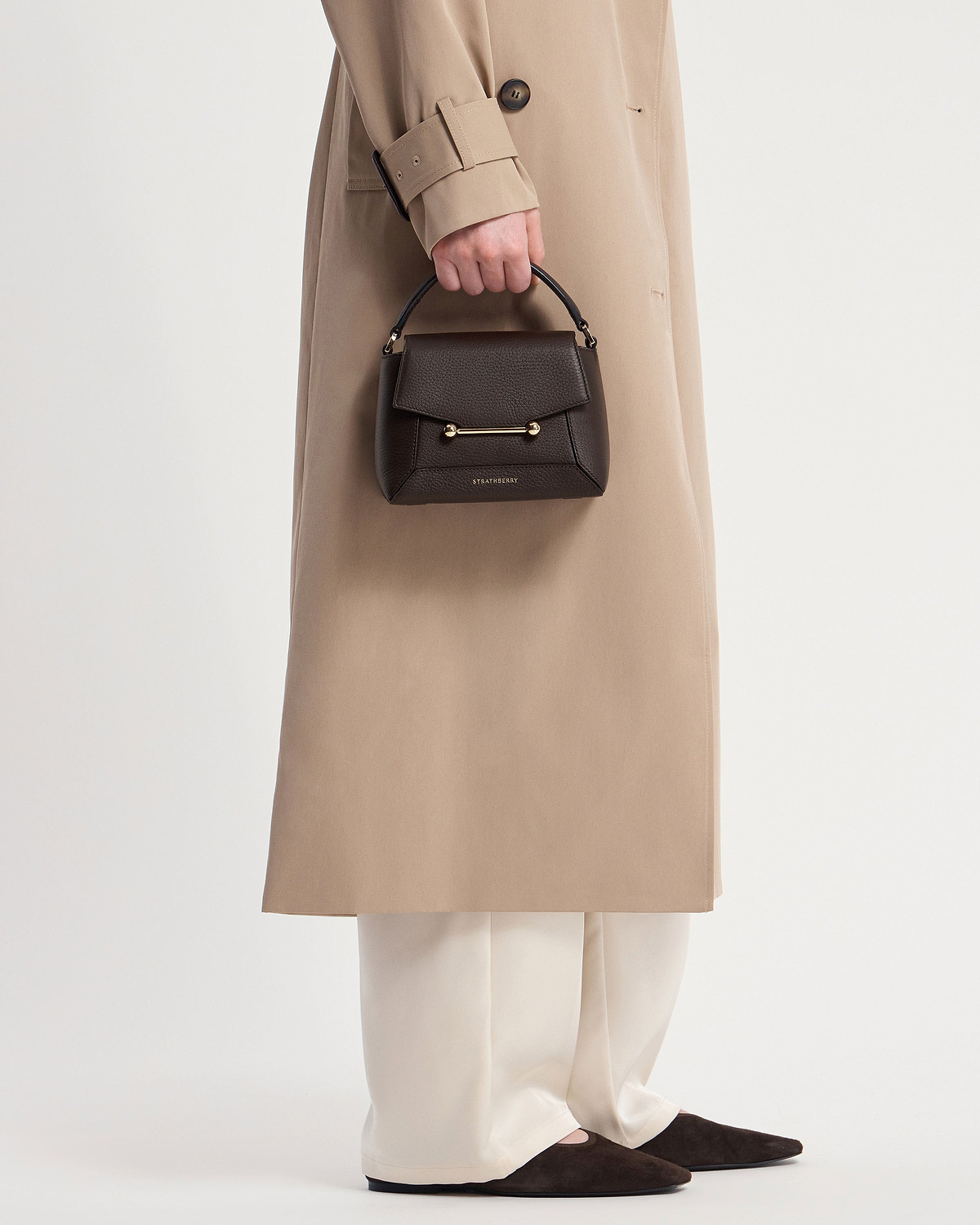 Model holding Strathberry Mosaic Nano bag in espresso with top handle and gold bar