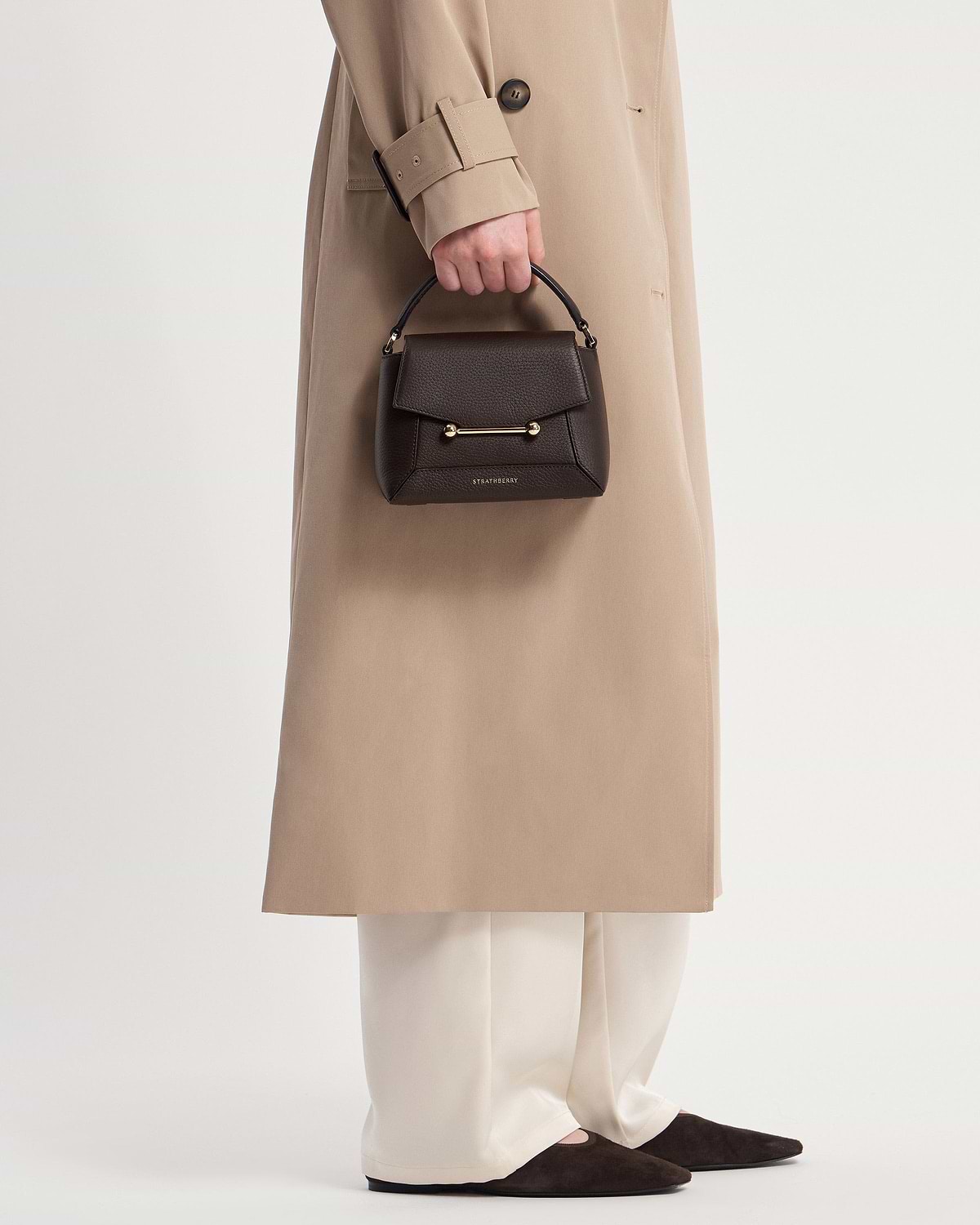 Model holding Strathberry Mosaic Nano bag in espresso with top handle and gold bar