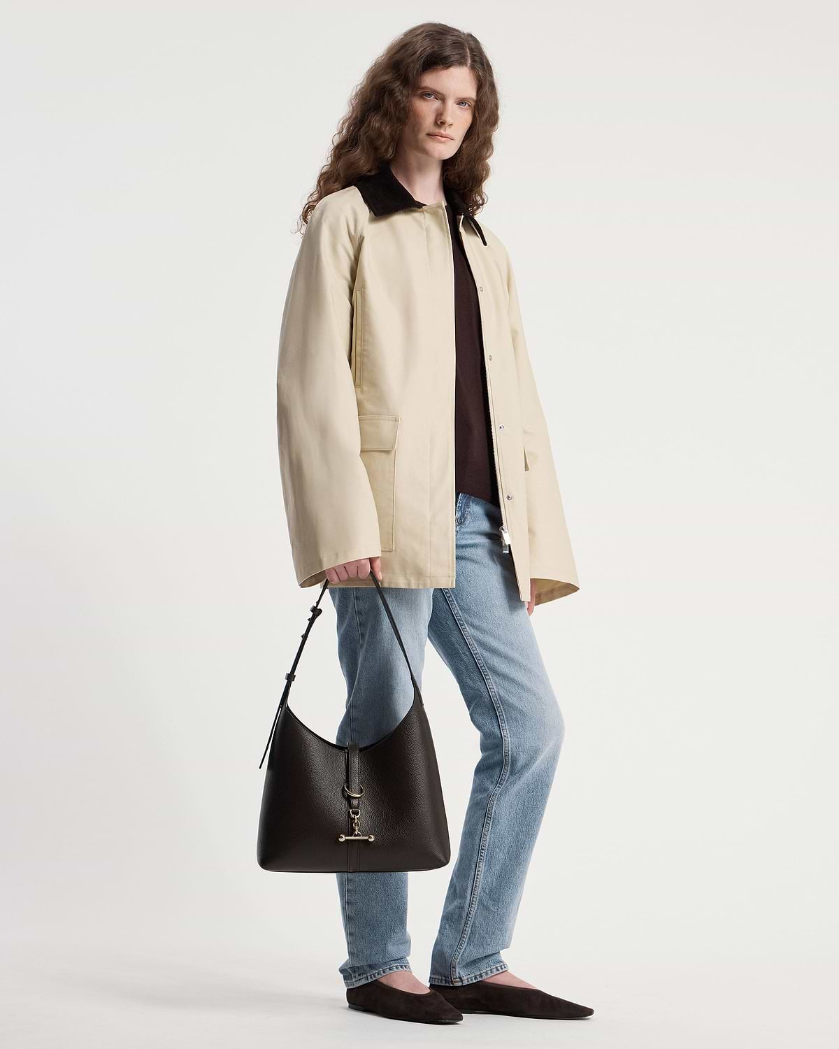 Model holding an espresso leather Kite Hobo shoulder bag by the strap.