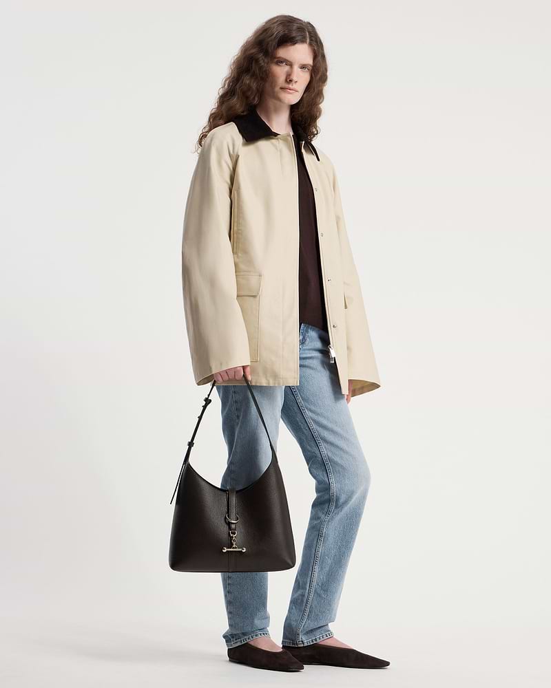 Model holding an espresso leather Kite Hobo shoulder bag by the strap.