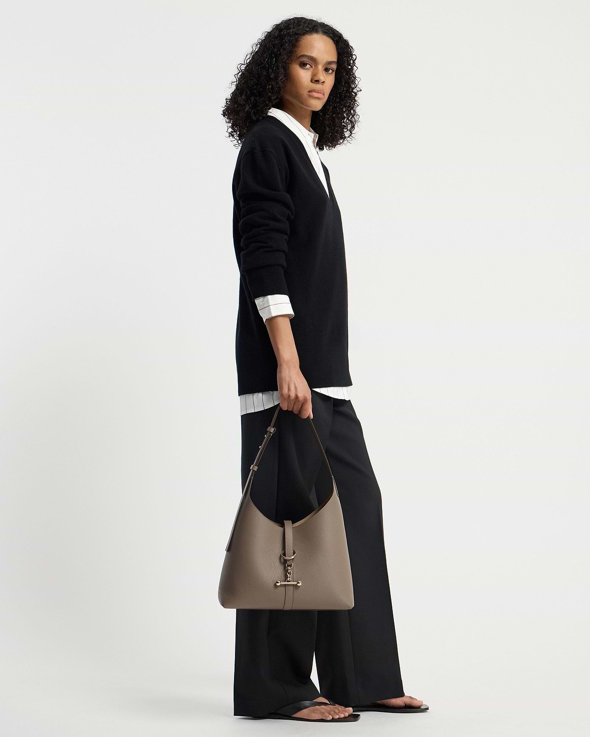 Model holding taupe Kite Hobo shoulder bag with gold T-bar hardware.