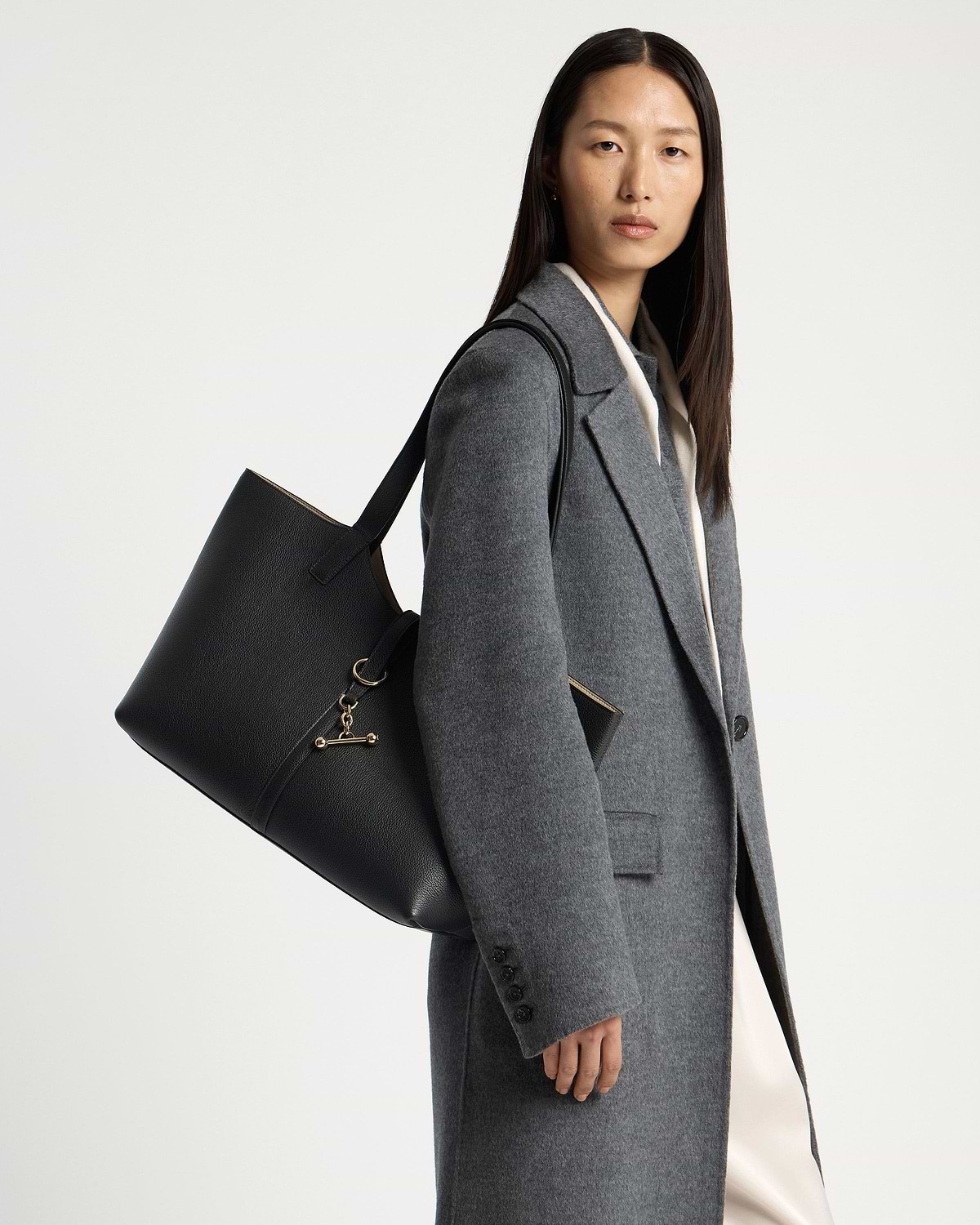 Model wearing a grey coat carrying a black kite tote shoulder bag