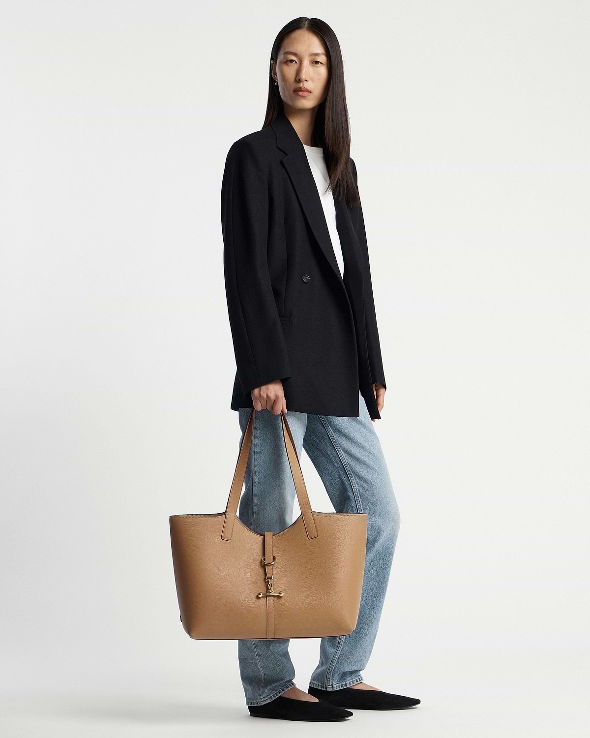 Model holding caramel tote with gold bar clasp, wearing blazer and jeans.