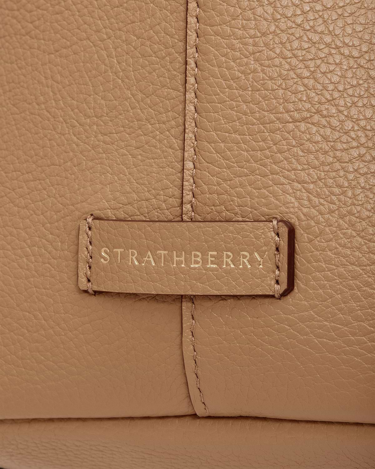 Caramel pebbled leather detail showing Strathberry logo on stitched tab of tote.