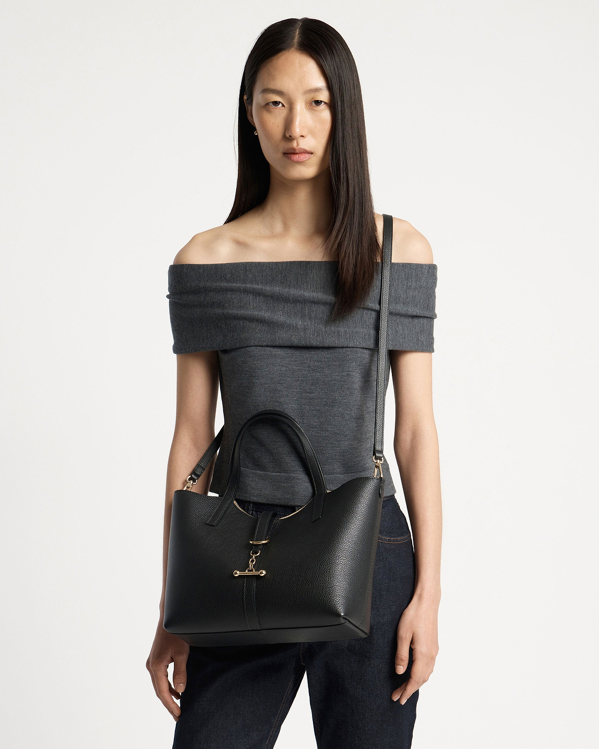 Woman wearing off-shoulder top carries black Kite Tote Midi with gold bar clasp.