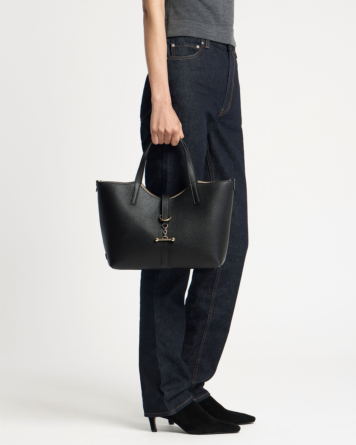 Model holding black pebbled leather tote bag with gold bar hardware by its handles