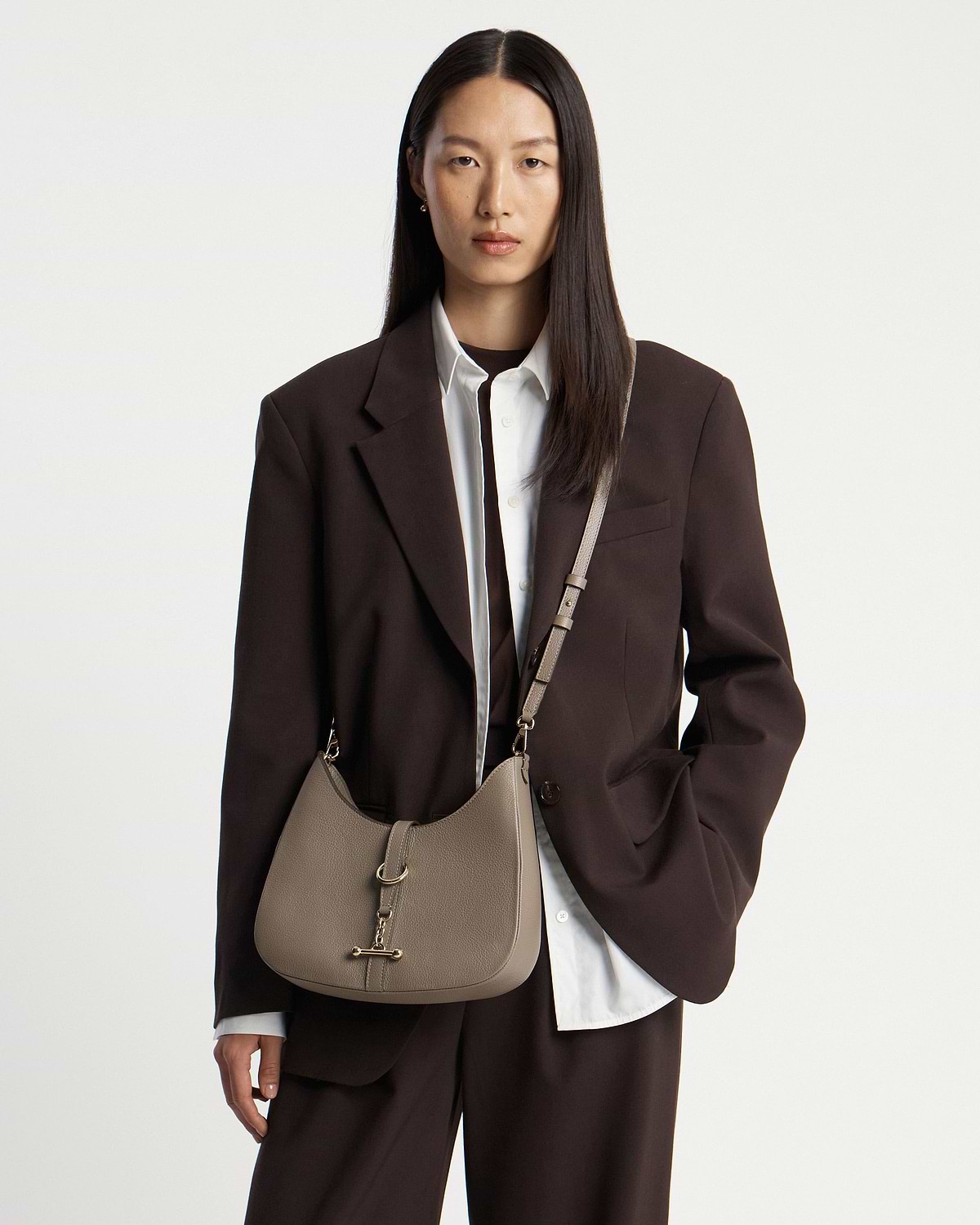 Model wearing taupe kite sling bag cross-body with gold hardware and dark blazer