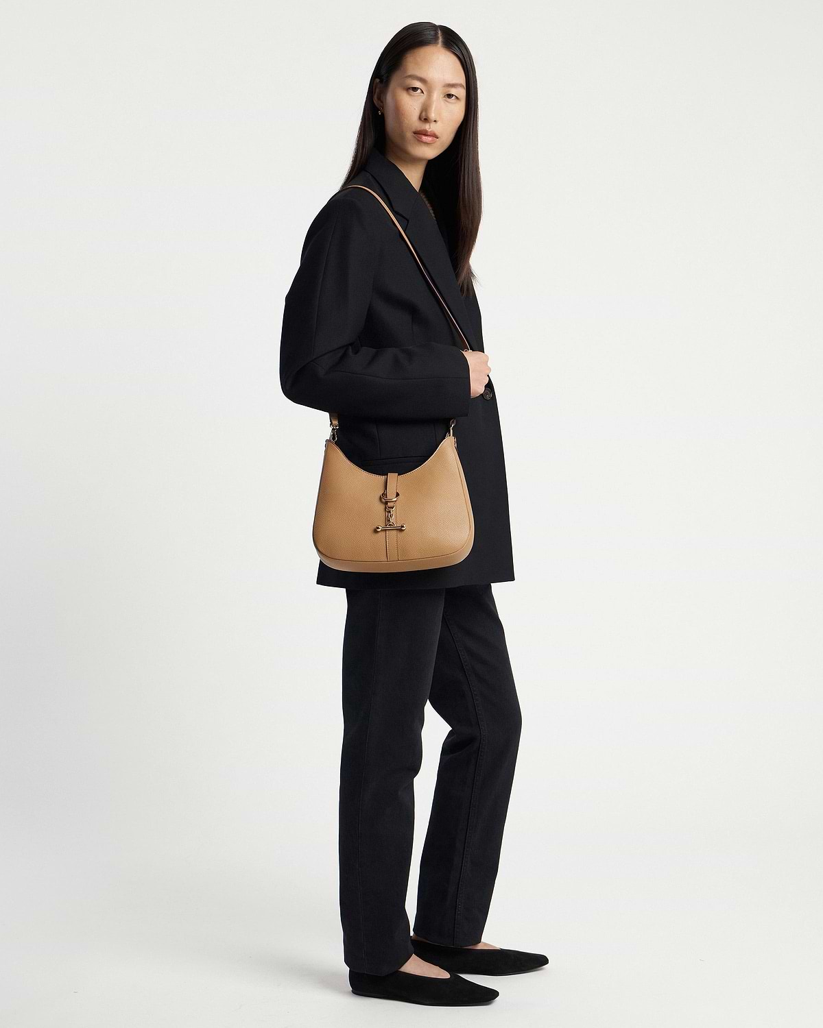 Model wearing caramel kite sling bag with shoulder strap and black blazer.