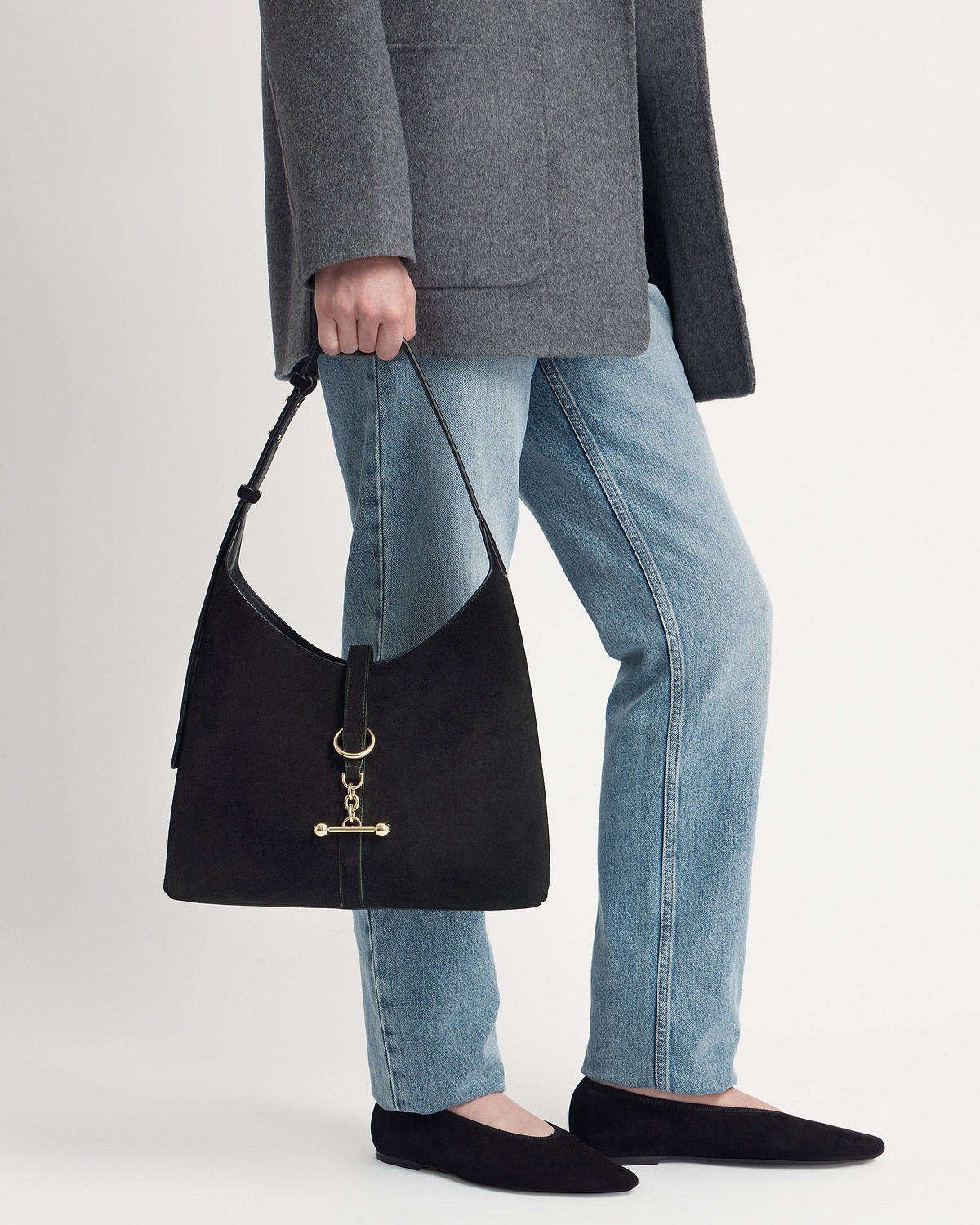 Model cropped below the waist holding a black suede Kite Hobo bag with gold hardware.