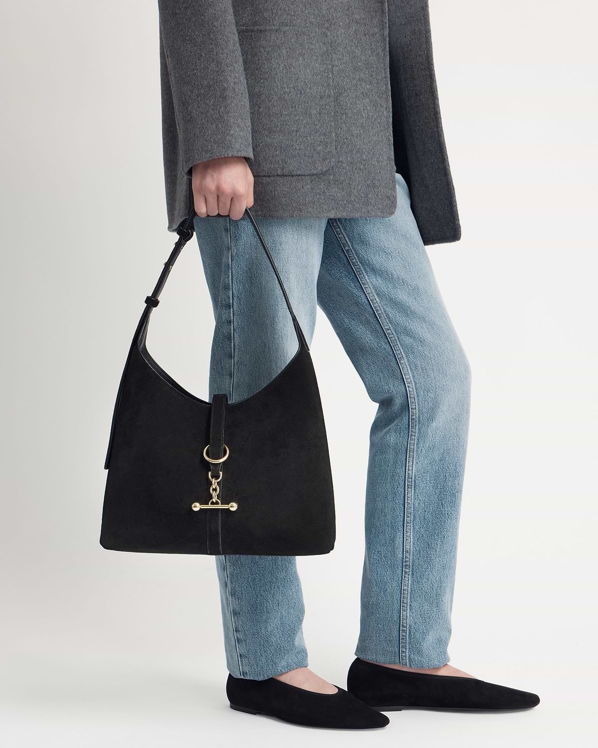 Model cropped below the waist holding a black suede Kite Hobo bag with gold hardware.