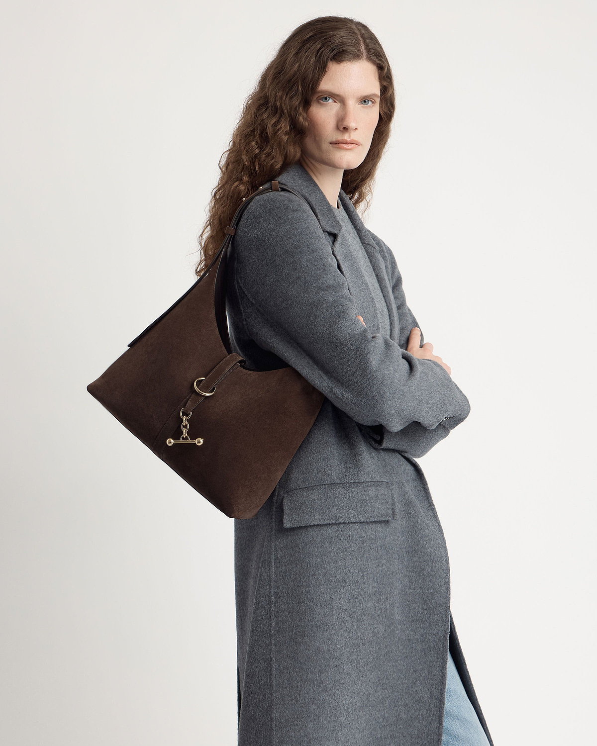 Model wearing chocolate suede Kite Hobo bag over shoulder, grey coat visible.