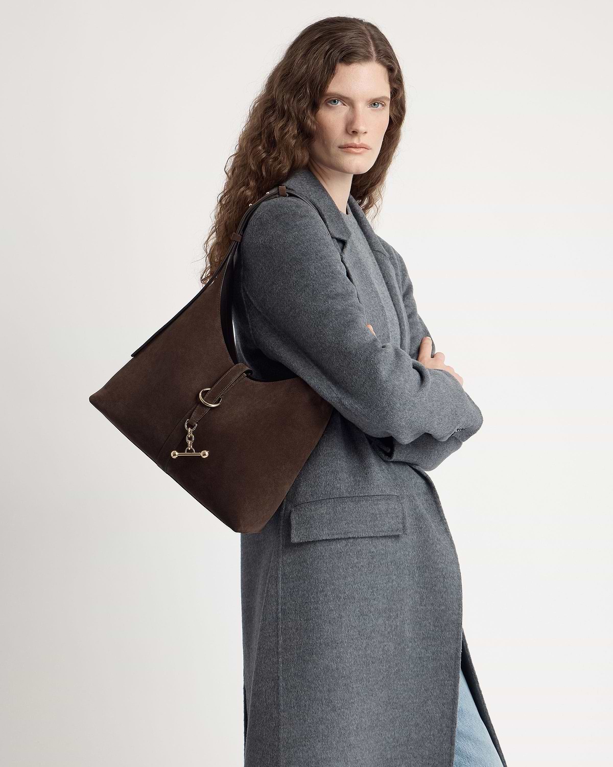 Model wearing chocolate suede Kite Hobo bag over shoulder, grey coat visible.
