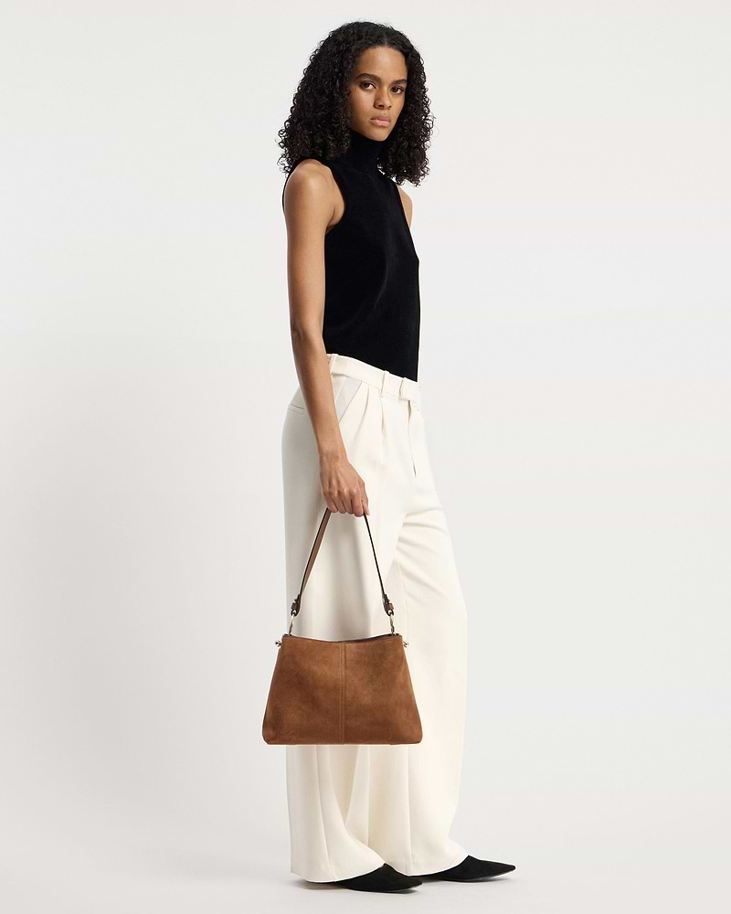 Model holding a tan suede hobo bag by its single shoulder strap.