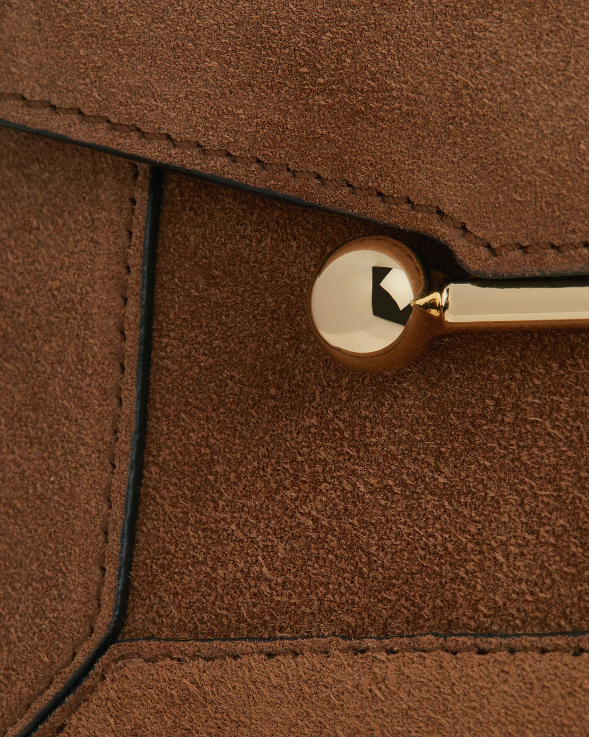 Close-up of tan suede bag panel showing gold metal stud and stitched edges.
