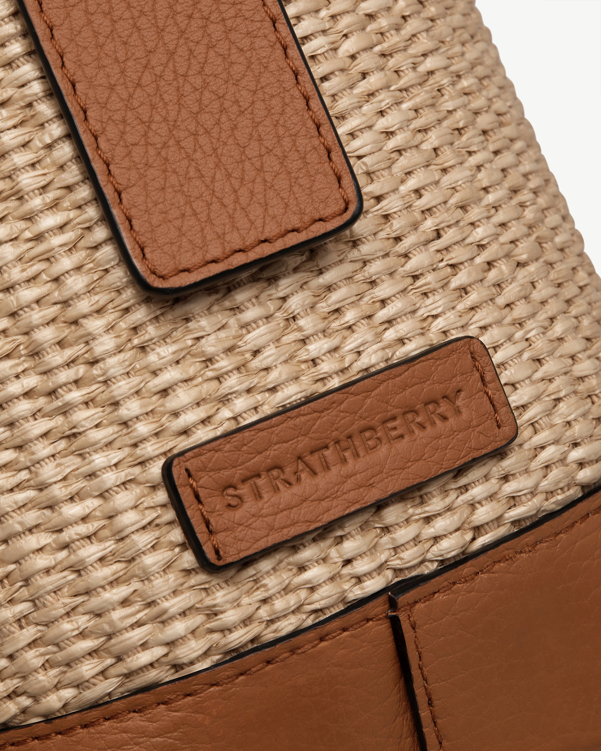 Tan leather patches on natural raffia weave with debossed Strathberry logo