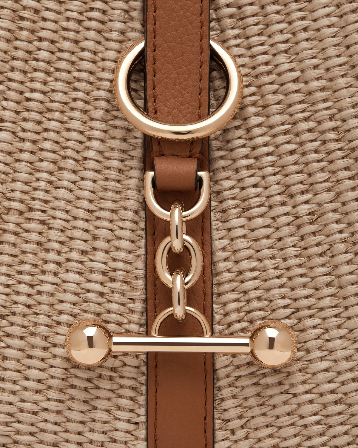 Tan leather strap with gold rings on natural raffia woven bag.