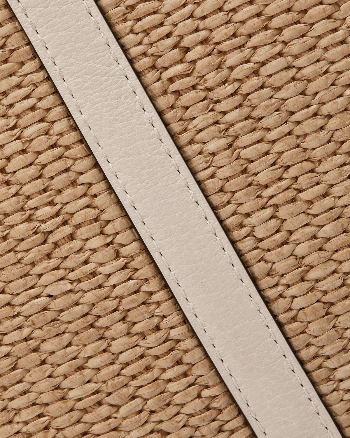 Vanilla leather strap across natural raffia weave on a hobo bag.