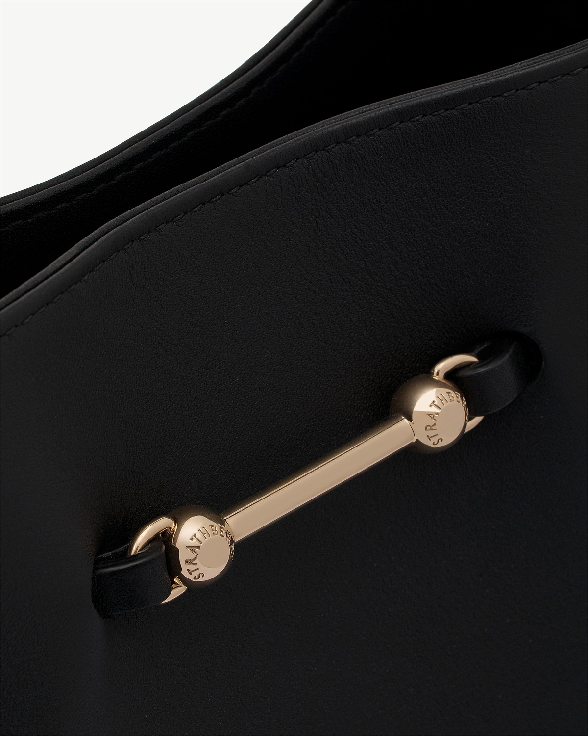 Black leather bag detail with gold Strathberry bar and stitching.