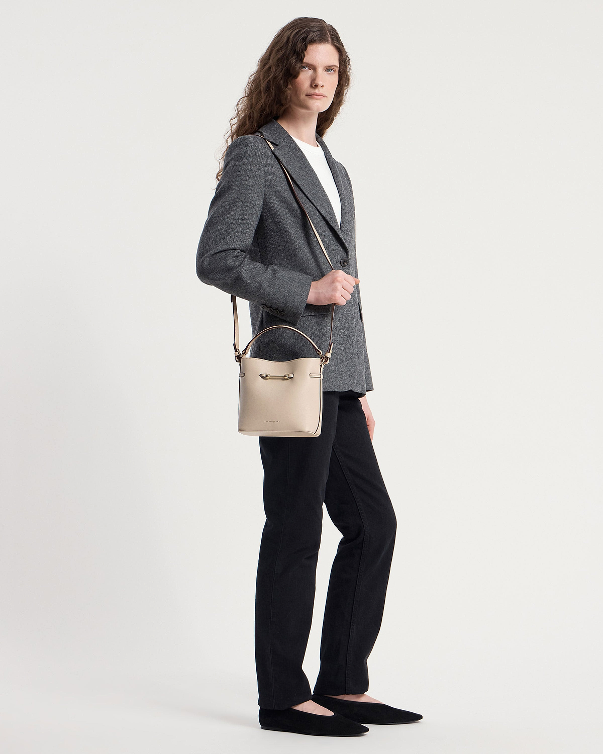 Model wearing grey blazer and black trousers holding oat bucket mini bag.