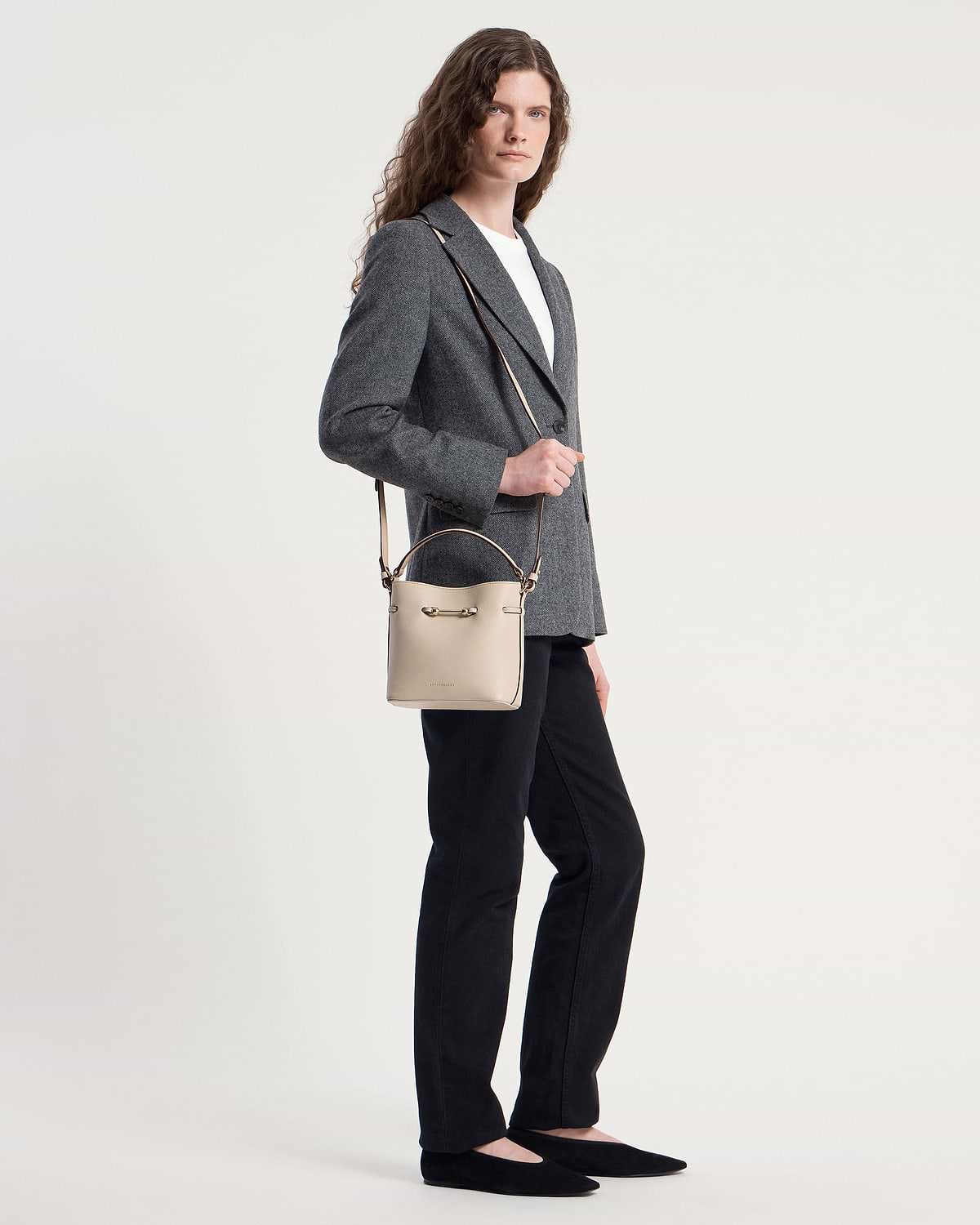 Model wearing grey blazer and black trousers holding oat bucket mini bag.