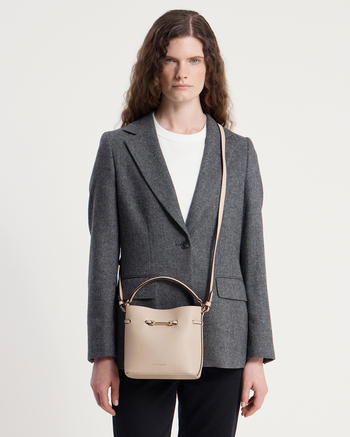 Woman wearing grey blazer with Strathberry Corda Bucket Mini in oat on shoulder