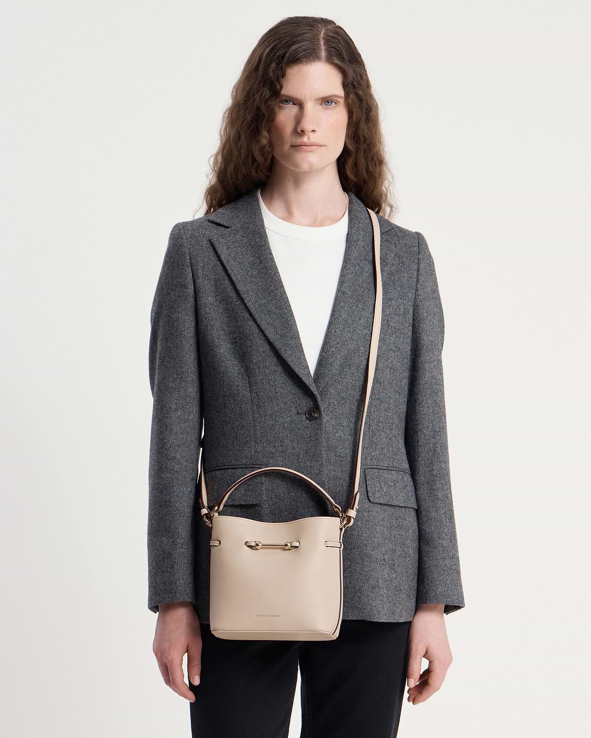 Woman wearing grey blazer with Strathberry Corda Bucket Mini in oat on shoulder