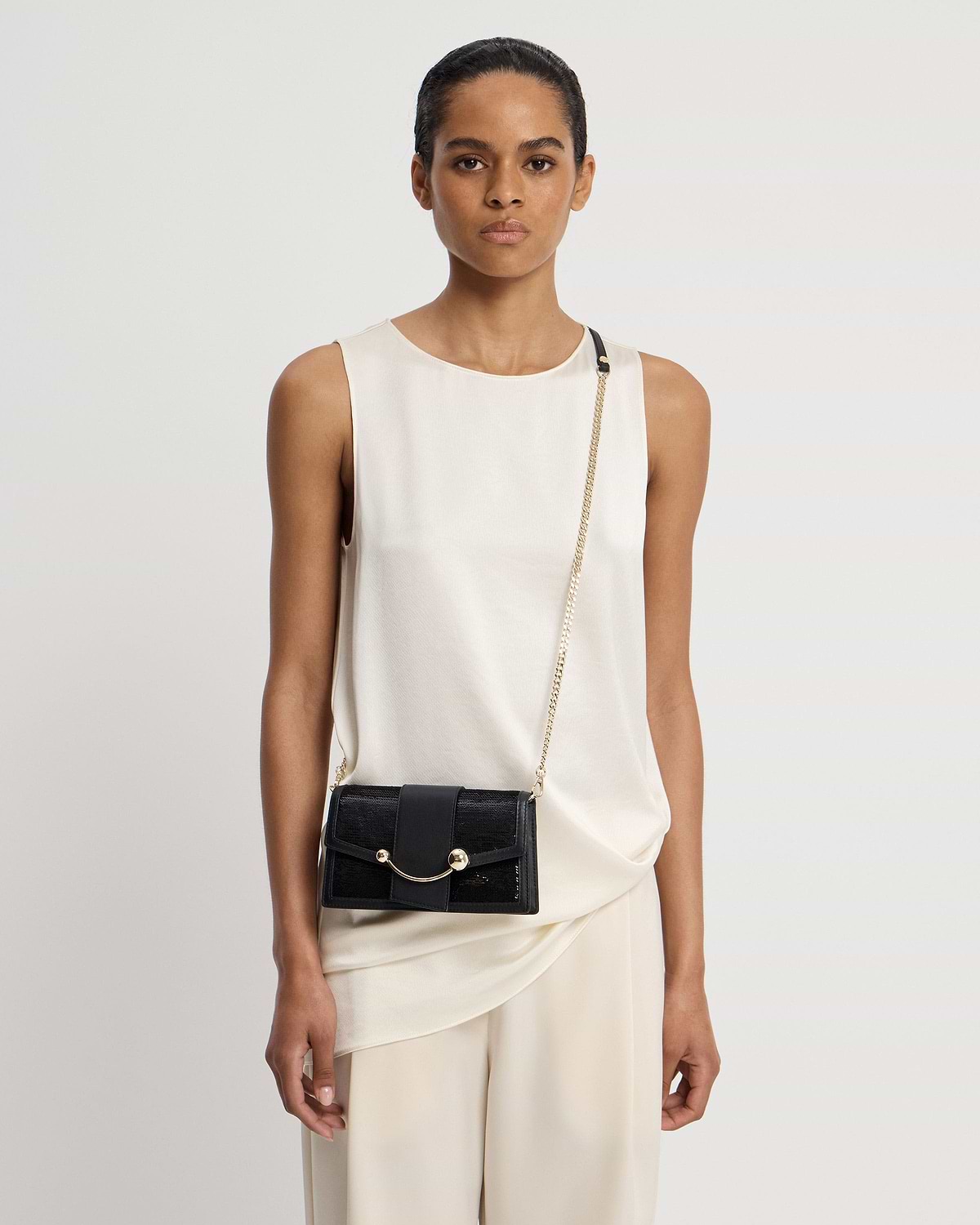 Model wearing cream sleeveless top with black sequinned crescent bag on gold chain.