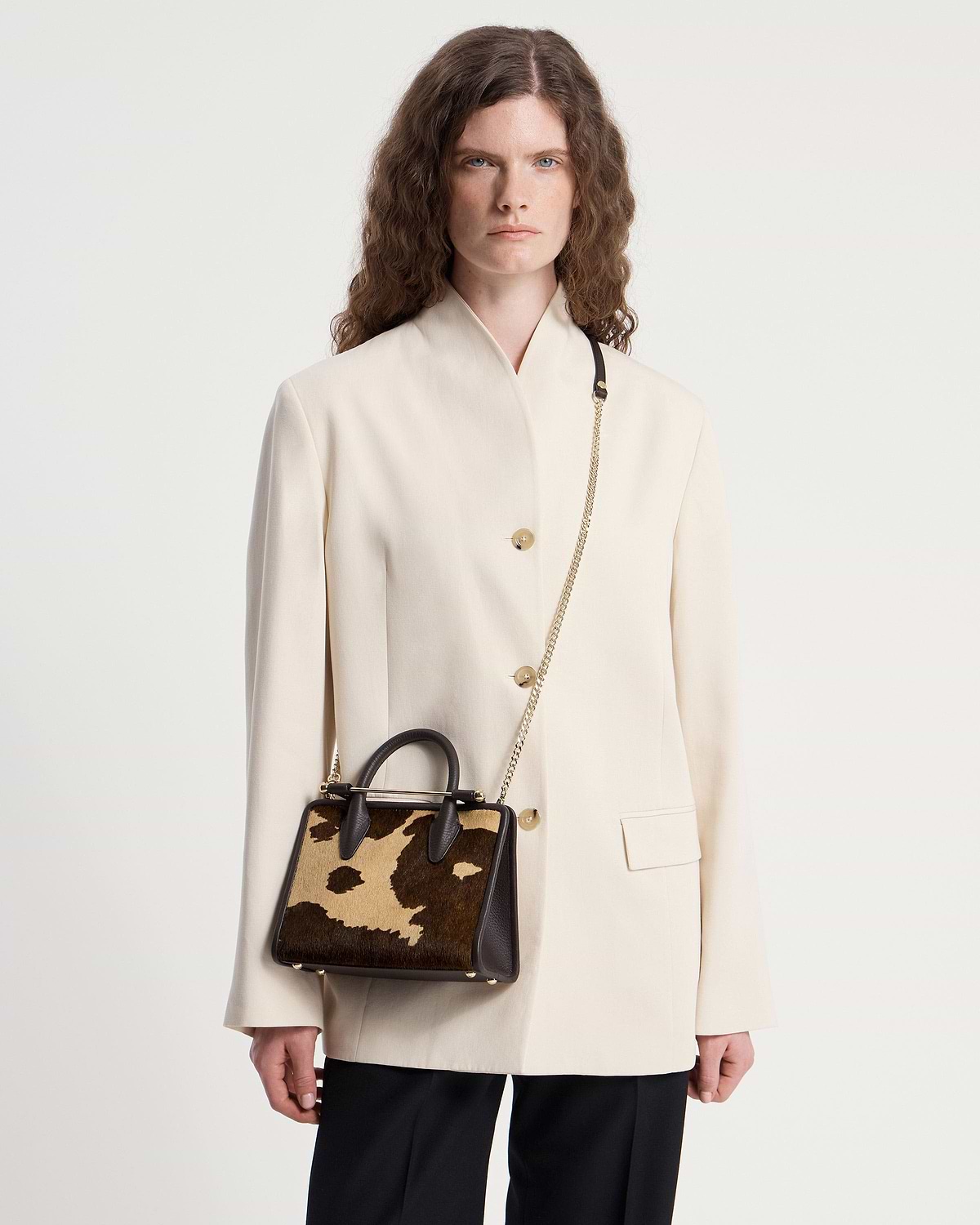 Model wearing cream blazer with mini tote in sand espresso spot print, gold chain strap.