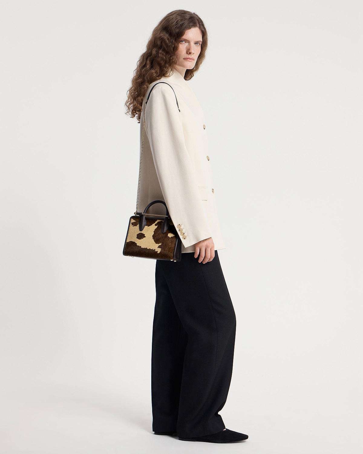 Model wearing cream blazer and black trousers holding sand and espresso spot-print mini tote bag.