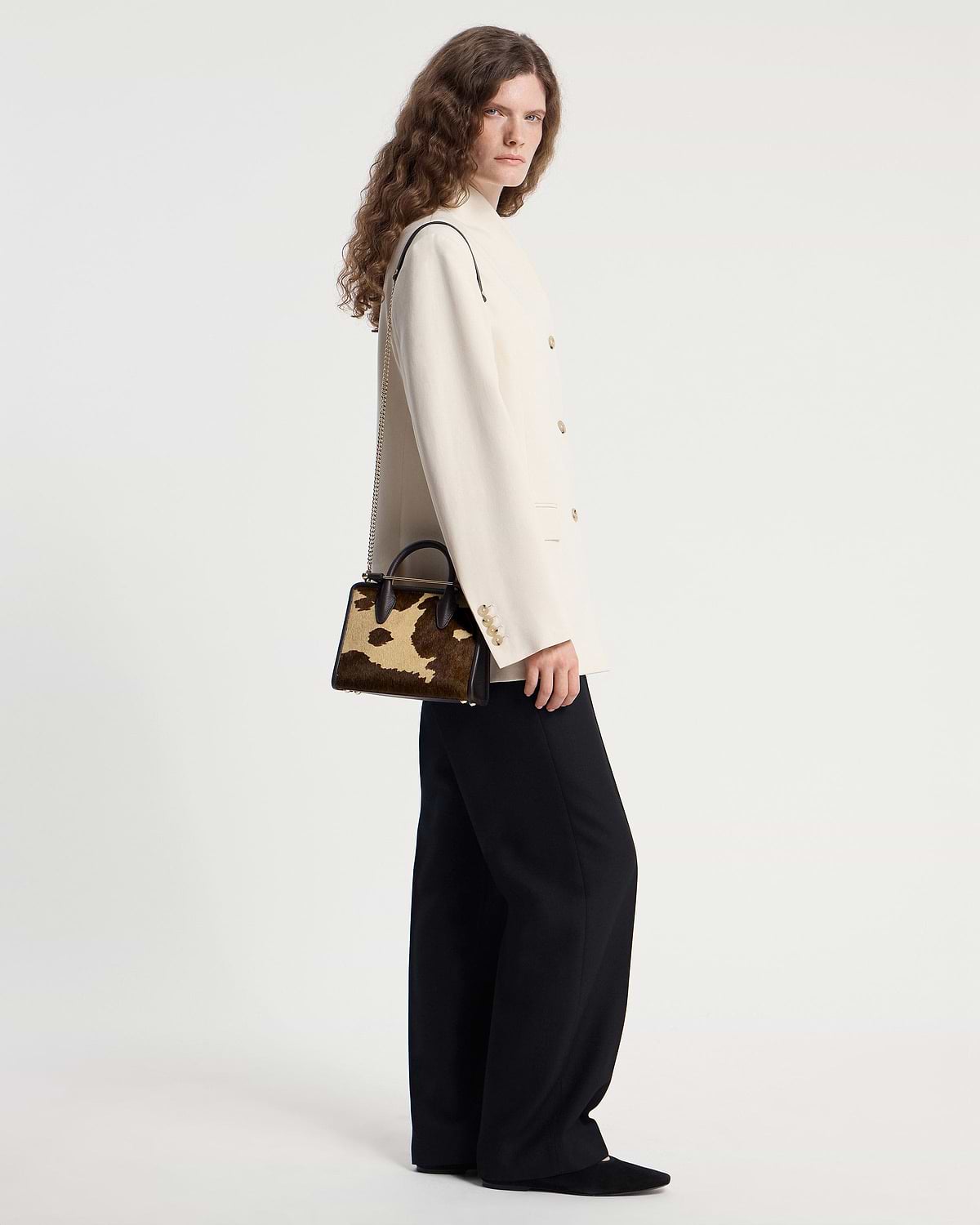 Model wearing cream blazer and black trousers holding sand and espresso spot-print mini tote bag.