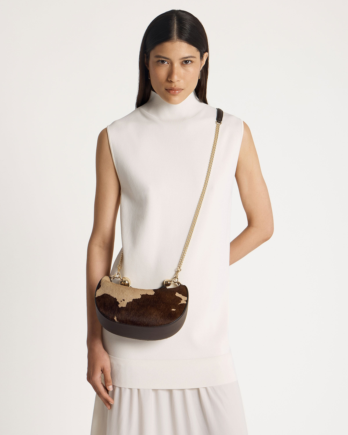 Model wearing crescent-shaped mini bag in sand and espresso spot print with gold chain strap.