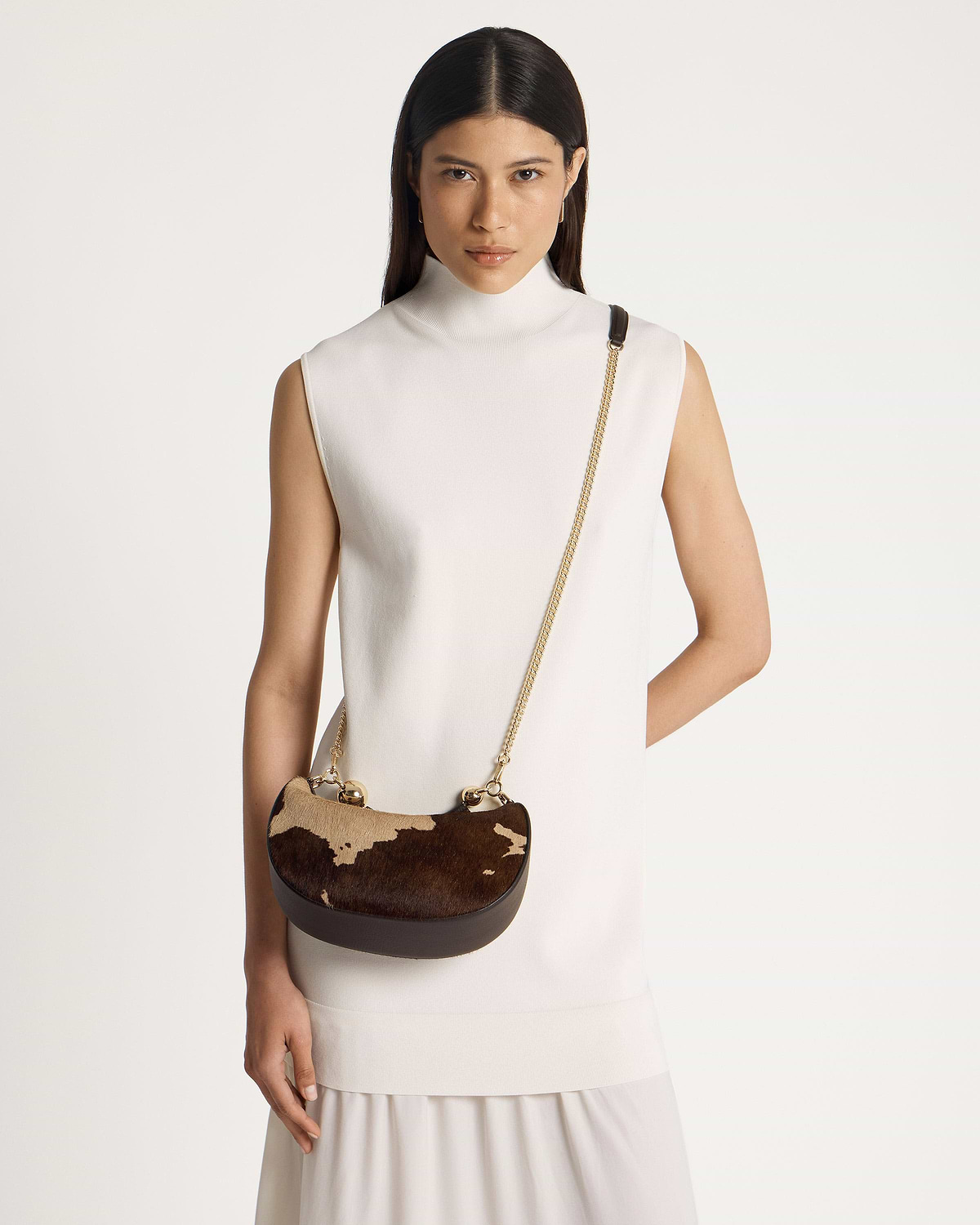 Model wearing crescent-shaped mini bag in sand and espresso spot print with gold chain strap.