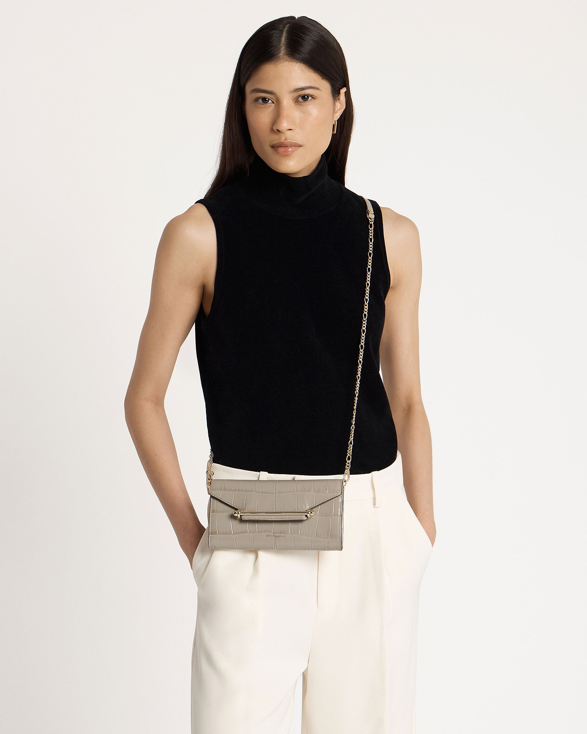 Model in a black sleeveless top and cream trousers with light grey croc-effect chain wallet.