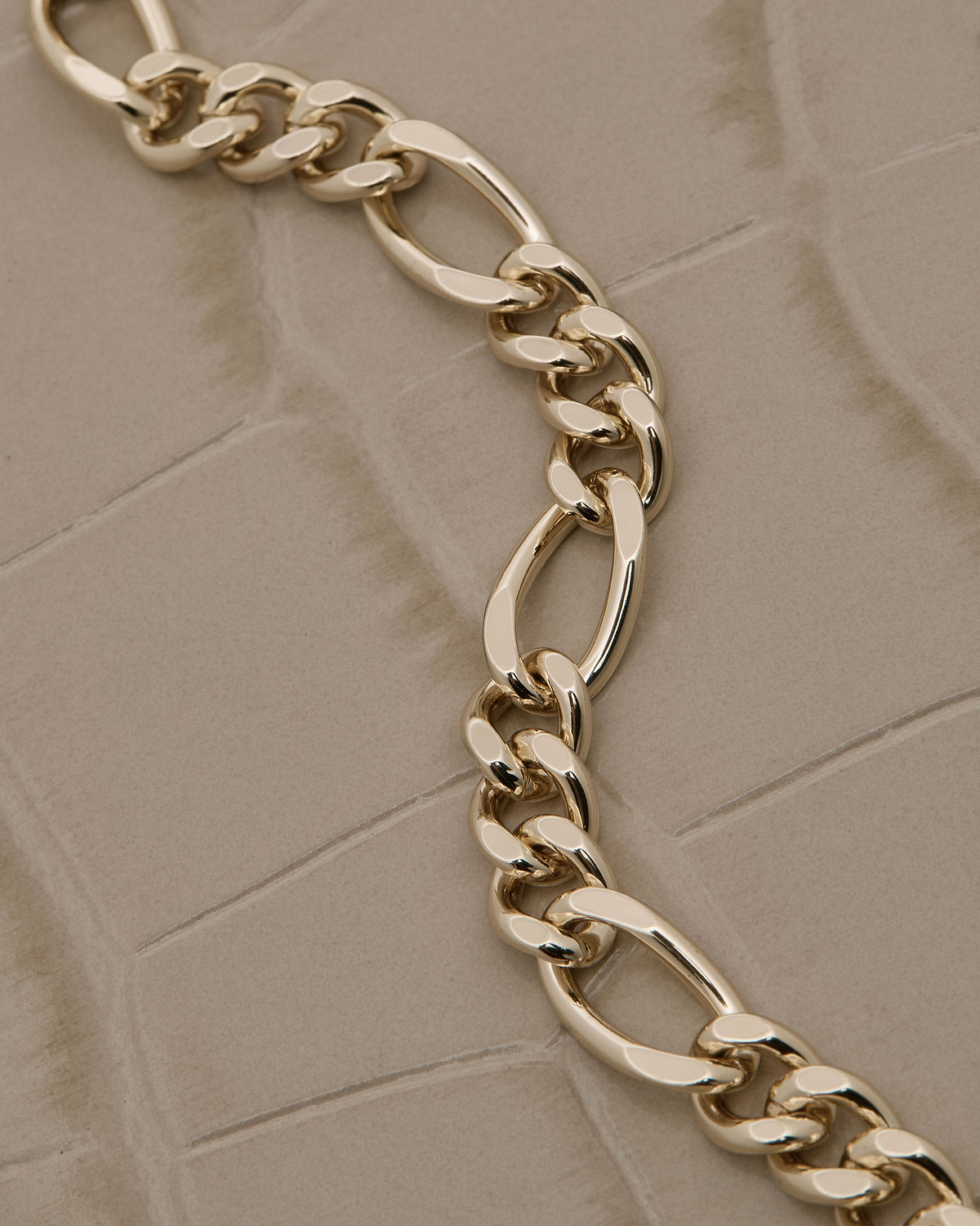 Gold chain strap laid across beige croc-embossed leather surface showing texture