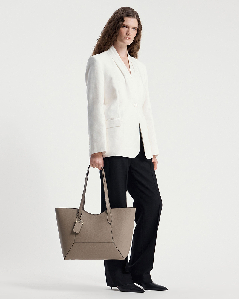 Model holding a taupe Mosaic Cabas tote with white blazer and black trousers