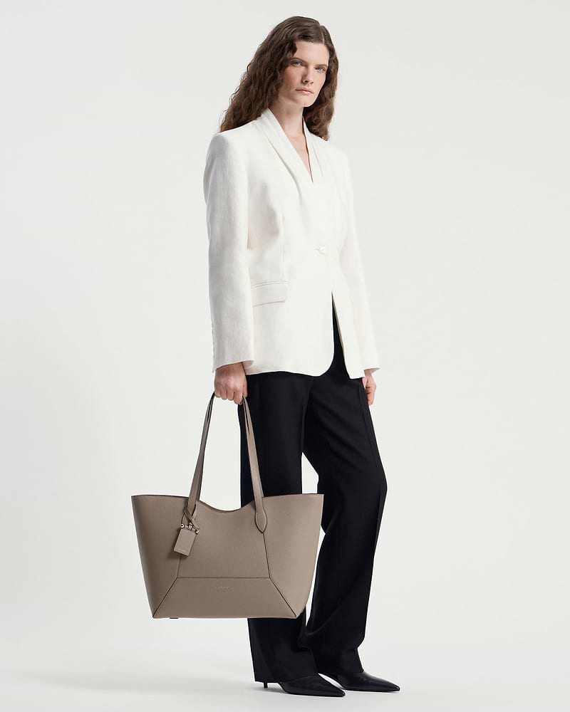 Model holding a taupe Mosaic Cabas tote with white blazer and black trousers