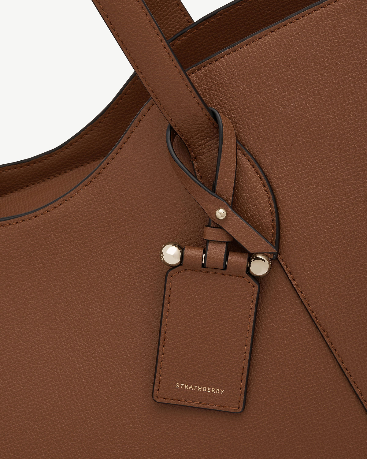 Hazelnut leather strap loop, gold studs and Strathberry logo on bag exterior.
