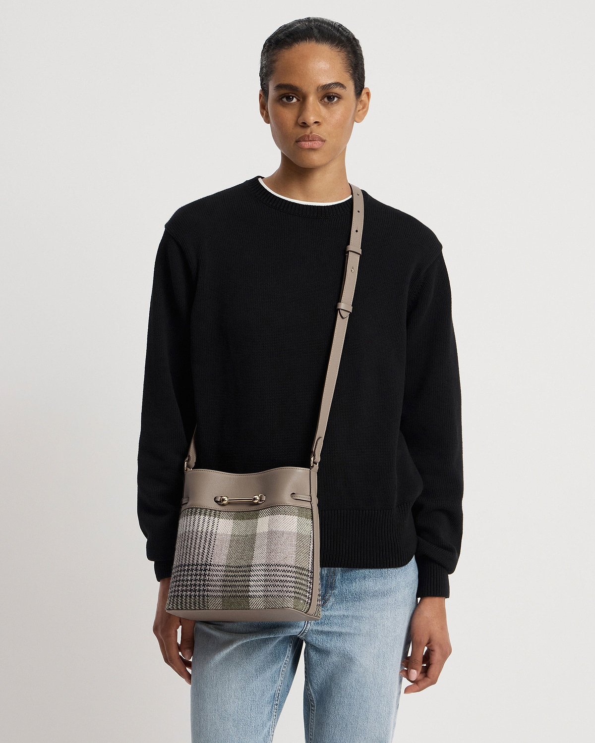 Model wearing taupe leather-strapped tartan bucket bag with gold bar detail across body