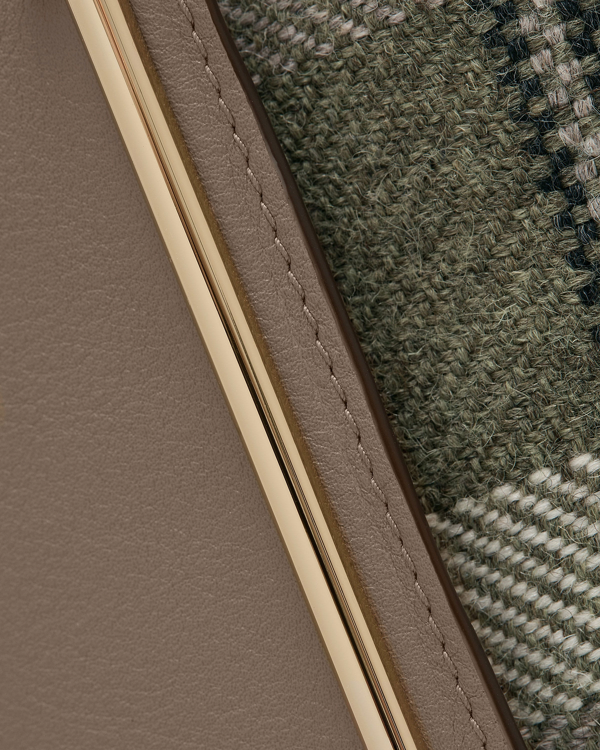 Taupe leather edge with gold metal trim beside green tartan woven fabric.