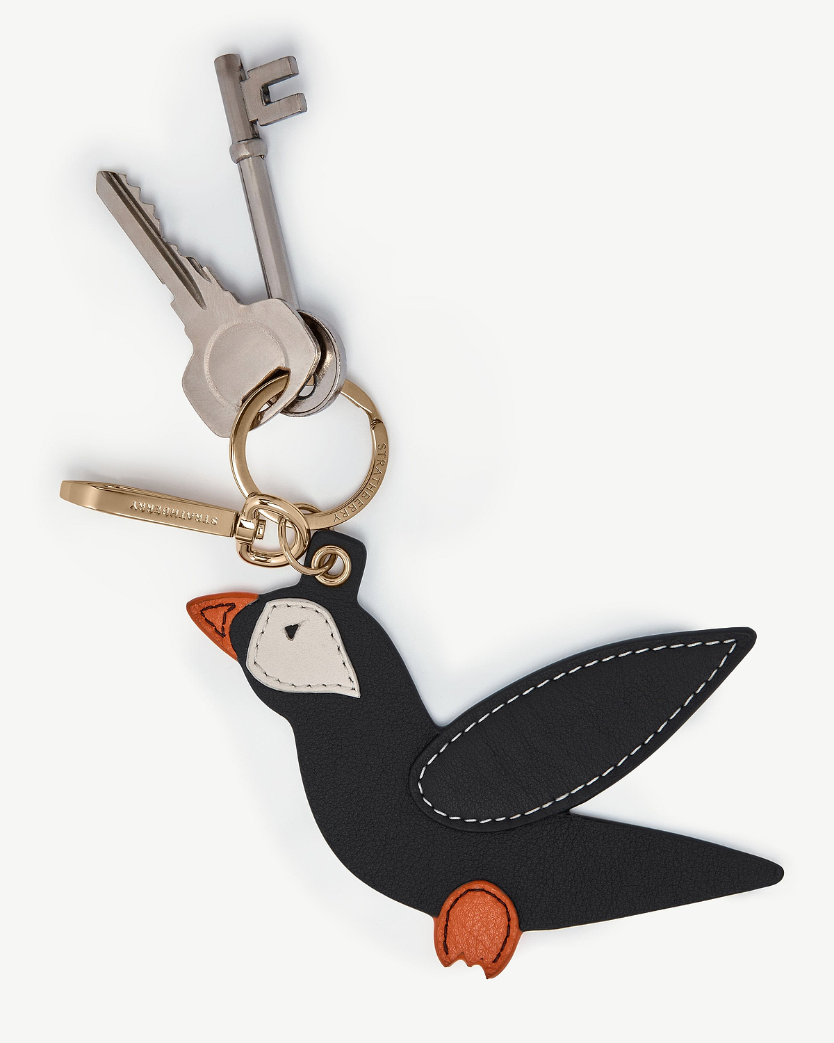 Strathberry black puffin bag charm with vanilla and marmalade details on gold keyring.