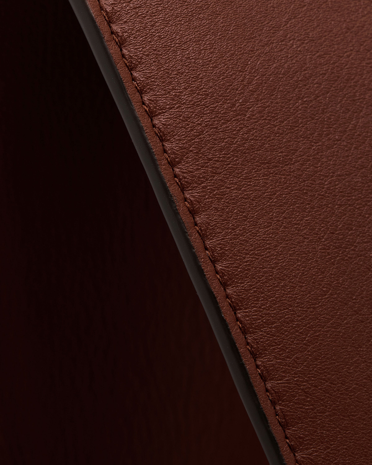 Walnut leather tote edge showing visible stitching and textured surface.