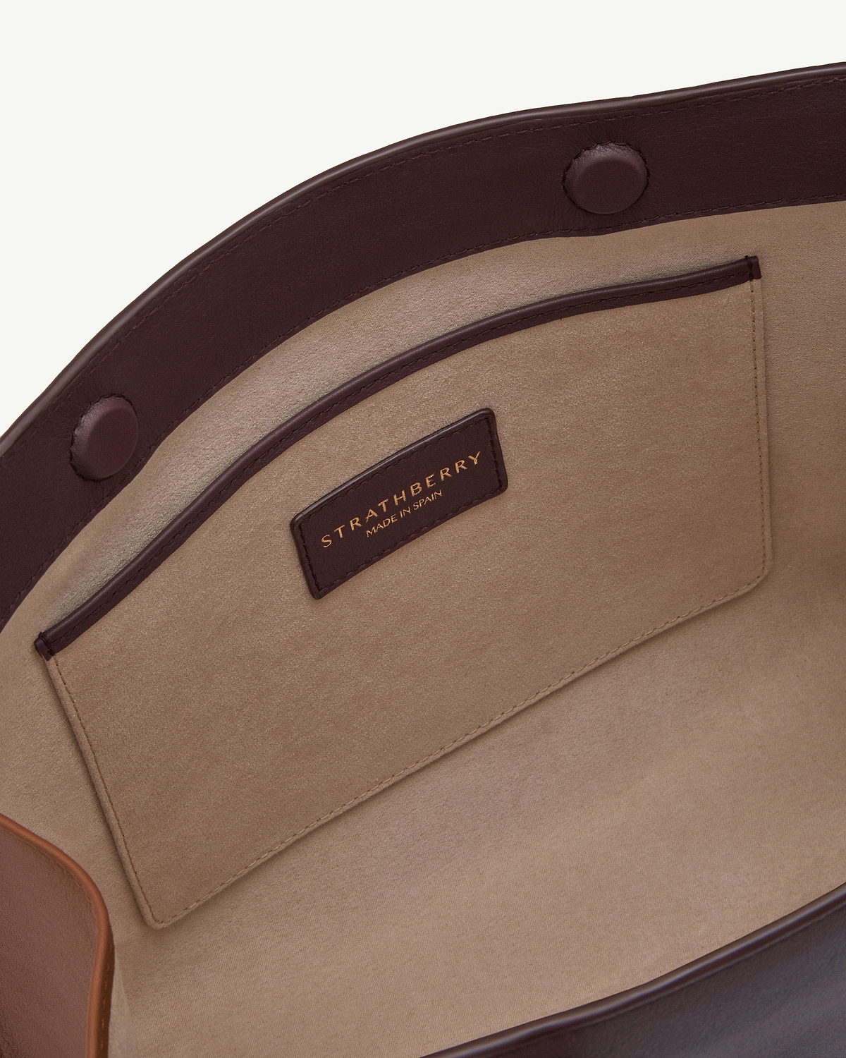 Interior of tote with burgundy leather trim, beige suede lining and Strathberry label