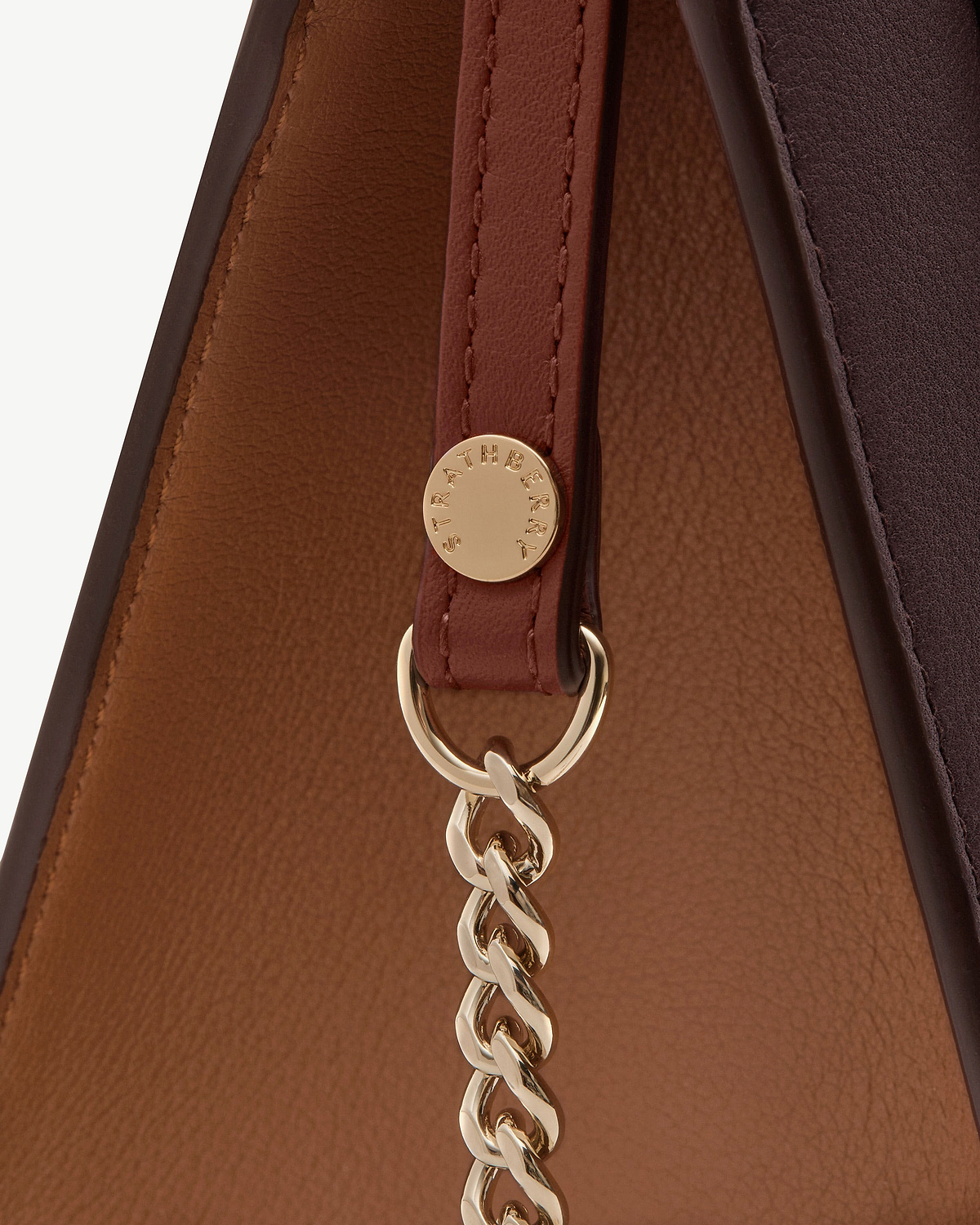 Close-up of burgundy mini tote strap and gold chain with Strathberry logo.