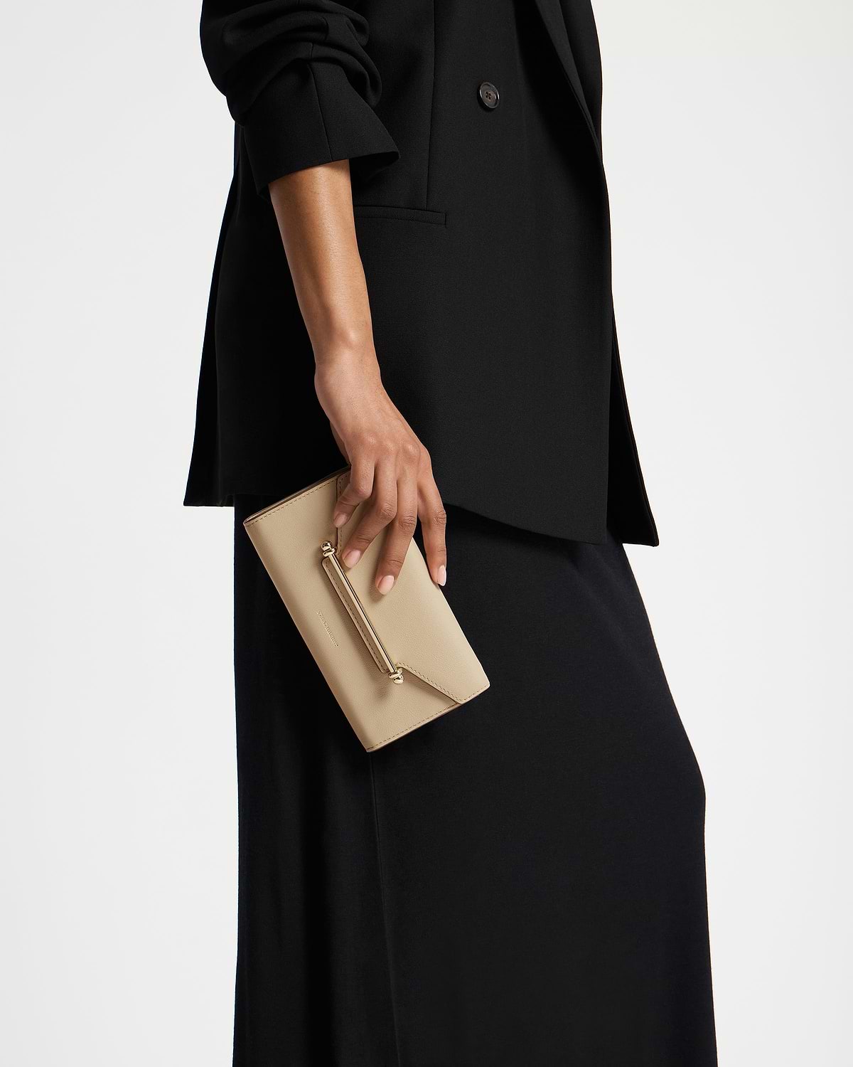 Hand holding sand leather wallet with gold bar detail against black coat