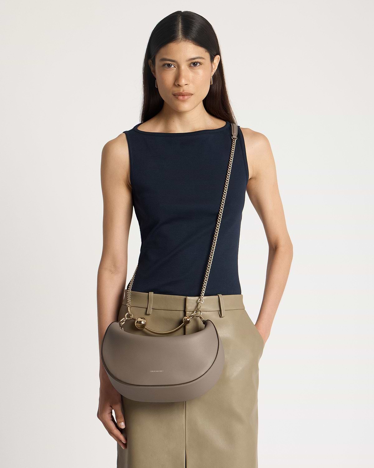 Model wearing navy top and taupe Strathberry Crescent Moon bag with gold chain strap.